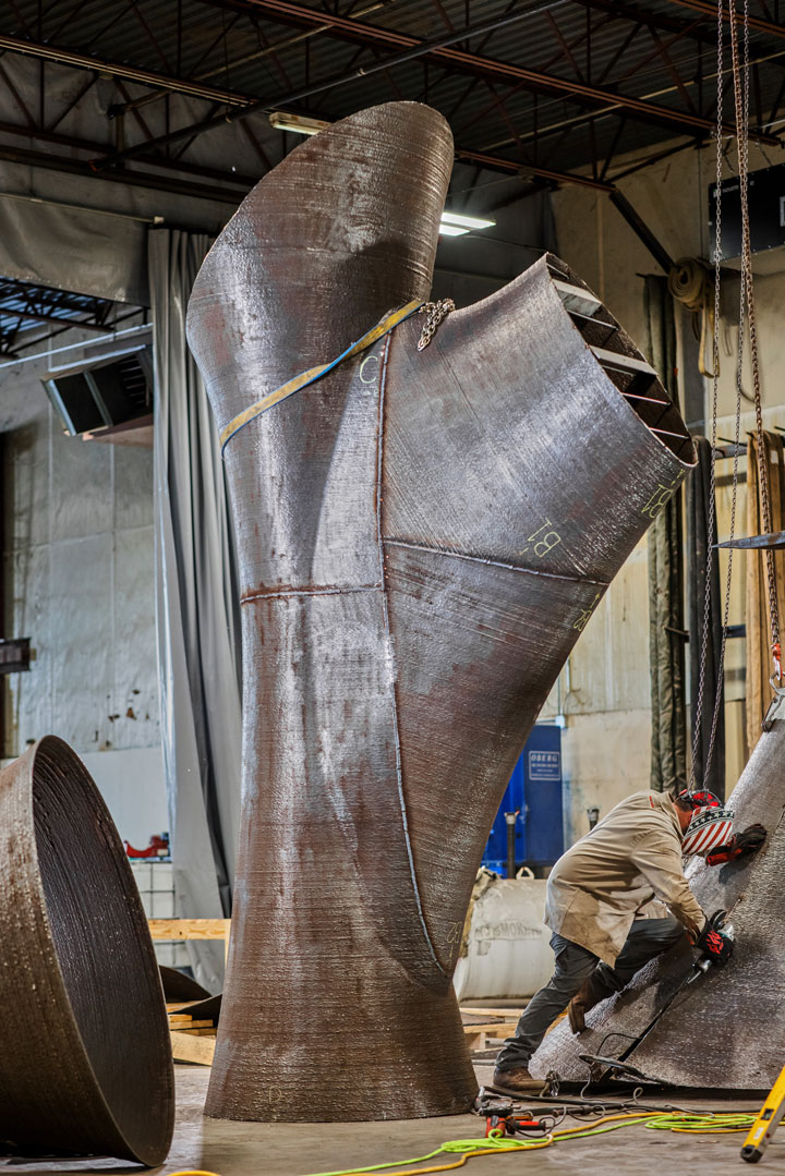 A fabricator grinding a large custom 3D-printed stainless steel sculpture