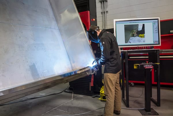 A welder using an automated positioning system to weld a large metal container for the heavy equipment industry