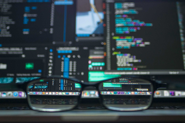 An information technology professional's glasses laying in front of a computer screen filled with code